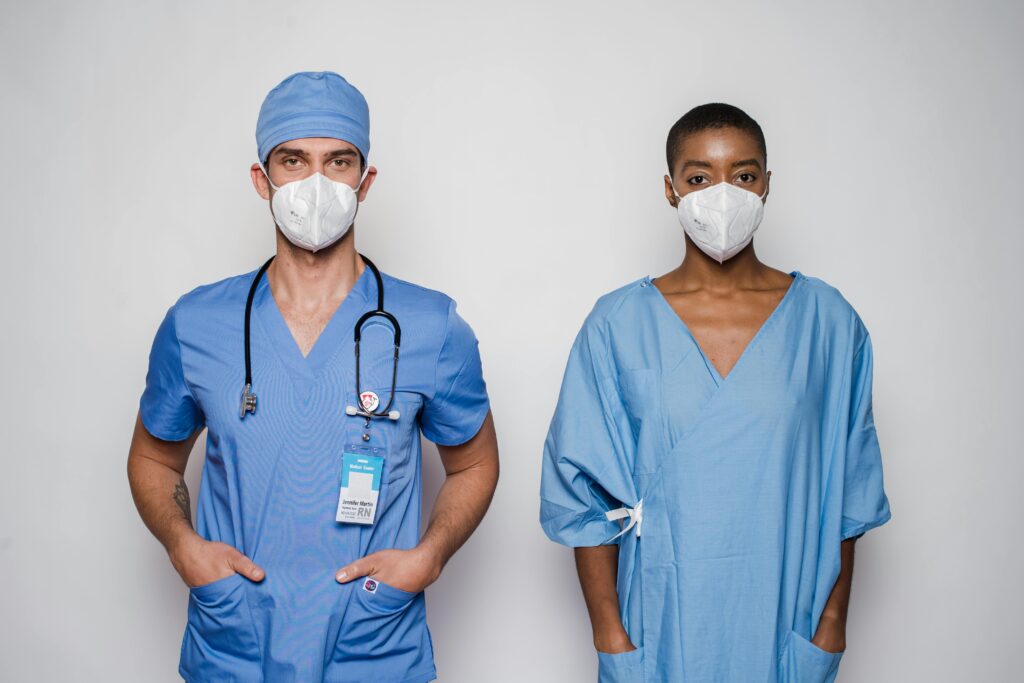 Two healthcare professionals in blue uniforms and masks standing together in a studio.